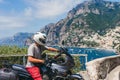 A motorbike traveler poses against the backdrop of an incredibly beautiful view of Positano, a city on the edge of cliffs, the sea