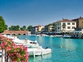 Motorboats anchored along the peschiera del garda canal in lake garda, italy with local businesses in the background and flowers