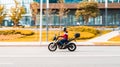 motorcycle rider on black and orange colored motorbike riding fast at city street in autumn