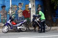 Motorcycle rider help a man fix his bicycle along a sidewalk of a road