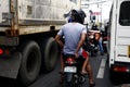 Motorcycle riders with passengers squeeze in between big vehicles at traffic congested road