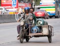 Motorcycle sidecar carrys gas tank driving on street.