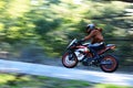 Motorcyclist in a brown hoodie aboard a KTM RC390 riding past on a mountain road