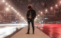 A motorcyclist in helmet stands among many lanterns. A lot of light effects. Middle of the light street. Night city. Snowfall in