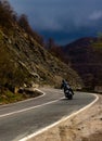 Motorcyclist moving on a motorcycle on a curved mountain road, in a stormy weather; motion blur caused by high speed crossing; the