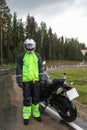 Motorcyclist traveler portrait wearing black and yellow raincoat and standing with motorbike on highway at rain weather