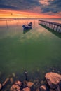 Motorized fishing boat tied to the shore near a pontoon and birds flying above it at sunrise on a lake Royalty Free Stock Photo