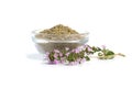 A mound of dried thyme grass in a glass bowl and a flowering branch of a medicinal thyme plant on a white background