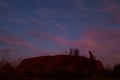 Mount Uluru at night. Stars in the sky and pink clouds. Eroded rock, orange color. Low bushes in front. Northern Territory NT,