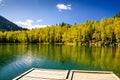 Mountain autumn green siberia lake with reflection, wooden pier and birch