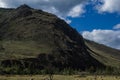 Mountain on Baikal, Sarma. Large tall green grassy round rock. Trees and bushes in the foreground in dry steppe. Cloudy blue sky