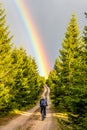 Mountain bike cycling after rain. Woman rides towards bright rainbow through forest country road. Outdoor sport theme Royalty Free Stock Photo