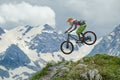 Mountain biker defies gravity, soaring mid-air against backdrop of snow-capped peaks and lush greenery Royalty Free Stock Photo