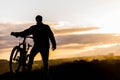 Mountain biker standing on top of a mountain with a bicycle, a beautiful sunset. Silhouette of a cyclist