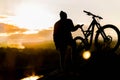 Mountain biker standing on top of a mountain with a bicycle, a beautiful sunset. Silhouette of a cyclist