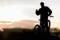 Mountain biker standing on top of a mountain with a bicycle, a beautiful sunset. Silhouette of a cyclist