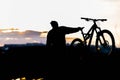 Mountain biker standing on top of a mountain with a bicycle, a beautiful sunset. Silhouette of a cyclist