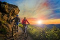 Mountain biking women and man riding on bikes at sunset mountain