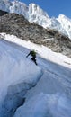 Mountain climber crosses over a large and deep crevasse or bergschrund as he begins his climb of a steep north face of ice and sno Royalty Free Stock Photo