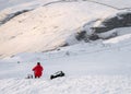 Mountain climber in red coat on white snow covered mountain hill taking break to keep warm eat and drink. Looking at hillside Royalty Free Stock Photo