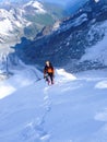 Mountain climber standing high up on a narrow and exposed snowy mountain ridge under a blue sky with tracks leading up Royalty Free Stock Photo