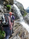 Mountain climbers hiking under a waterfall on a rocky hiking trail