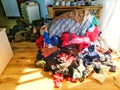 A mountain of colorful clothes in front of a chest of drawers on the bedroom's hardwood floor