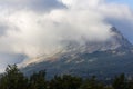 A mountain covered in clouds with a few trees in the foreground Royalty Free Stock Photo