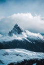 a mountain covered in snow under a cloudy sky with clouds in the background and a few trees in the foreground Royalty Free Stock Photo