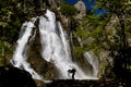 Among the mountains, great waterfall flowing in the canyon , the lake and the photographer taking them Royalty Free Stock Photo