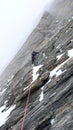 Mountain guide leading a steep rock climbing pitch on a hard mountaineering route in the Alps on an overcast and foggy day