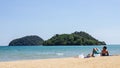 Mountain island over the sea with tourist lay down on the beach on the right side with bright sky in background in the afternoon. Royalty Free Stock Photo