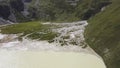 Mountain lake of beige or milky color in a valley. Clip. Aerial view of unusual white lake near green field at foot of