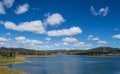 Blue calm deep water lake with gently sloping banks surrounded by hills with trees under a blue sky with small soft white clouds 1 Royalty Free Stock Photo