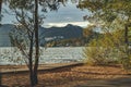 Mountain and lake through tree in foreground. Landscape with lake and mountains against blue sky. Fishing rods on lake against the Royalty Free Stock Photo