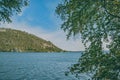 Mountain and lake through tree in foreground. Landscape with lake and mountains on background of blue sky Royalty Free Stock Photo