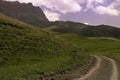 Mountain landscape - dark rocky bizarre cliff in bright sunny summer day with pink clouds in blue sky and country road Royalty Free Stock Photo