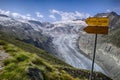 Mountain landscape with green fields and snowy peaks and wild glacier in the Swiss Alps and yellow hiking trail signpost with the Royalty Free Stock Photo