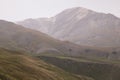 Mountain landscape - mountain peak with glacier in soft light white dim mist, yellow hilly folded slopes with dry alpine meadow