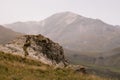 Mountain landscape - mountain peak with glacier in soft light white pastel dim mist, yellow hilly folded slopes with big boulder