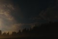 Mountain landscape pine trees near valley and colorful forest on hillside under blue sky with clouds and fog in moon light at Royalty Free Stock Photo