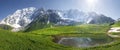 Mountain landscape of Svaneti on bright summer sunny day. Mountain lake, hills covered green grass on snowy rocky mountains