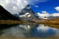 A mountain Matterhorn view partially covered by clouds and reflected in the smooth surface of the lake, in Switzerland