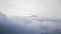 Mountain peak with a TV/radio relay on top, as seen above the clouds, on a cloudy Winter day with atmospheric inversion Royalty Free Stock Photo