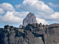 Mountain peak in white clouds. The peak rises among the white clouds. In the background a deep blue sky and the sun rising through