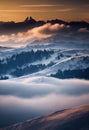 a mountain range covered in snow and clouds at sunset with a few clouds in the foreground and a few trees in the foreground Royalty Free Stock Photo