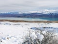 Mountain range covered by snow reflecting in the waters of a lake with snow on the foreground and grey cloudy sky Royalty Free Stock Photo