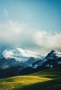 a mountain range with snow on the top of it and green grass below it and a blue sky with clouds Royalty Free Stock Photo