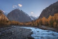 Mountain river on the background of autumn forest, snow capped mountains and blue sky