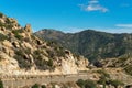 Mountain road in the afternoon sun with blue sky and few clouds with rock and stone formations on side of cliff Royalty Free Stock Photo